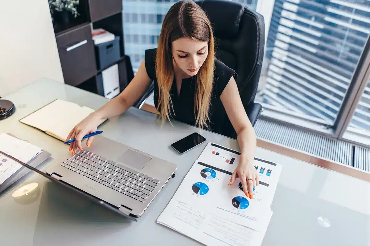 female businesswoman readind financial report analyzing statistics pointing at pie chart working at her desk female businesswoman readind financial report analyzing statistics pointing at pie chart working at her desk