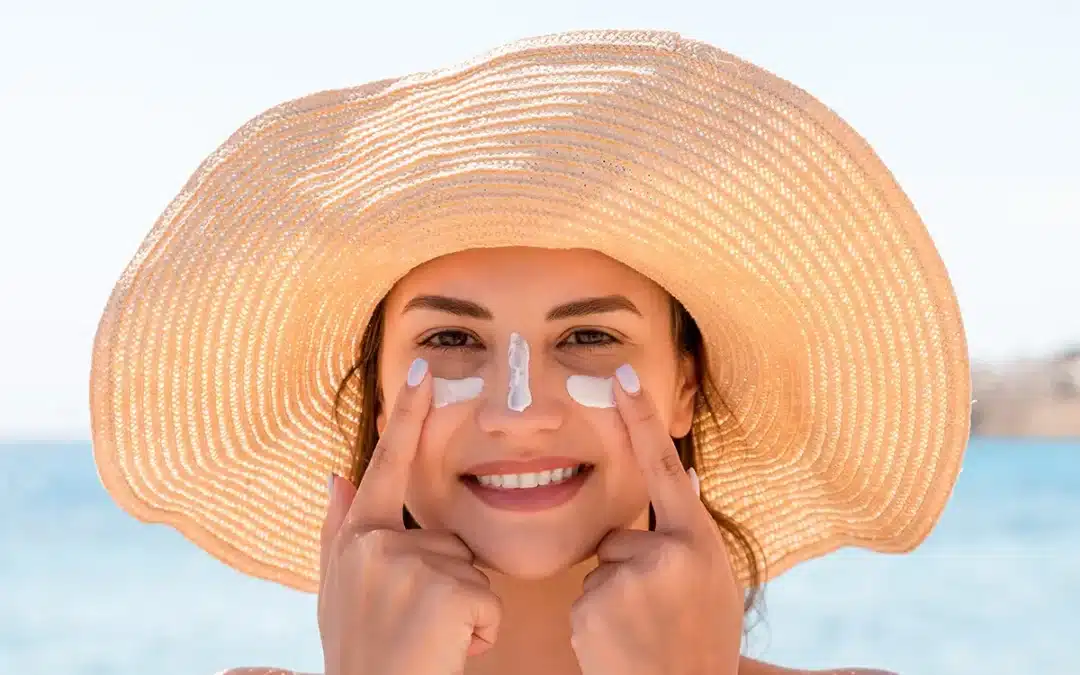 smiling woman in hat is applying sunscreen on her face