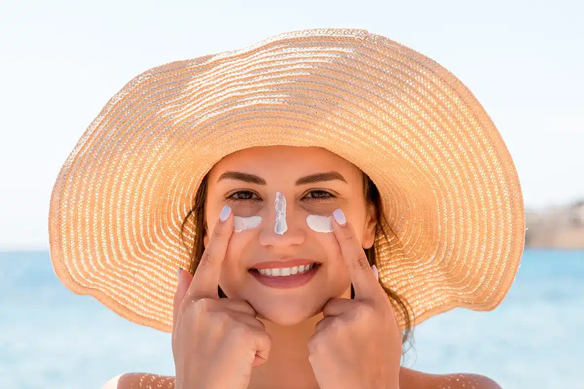 smiling woman in hat is applying sunscreen on her face smiling woman in hat is applying sunscreen on her face